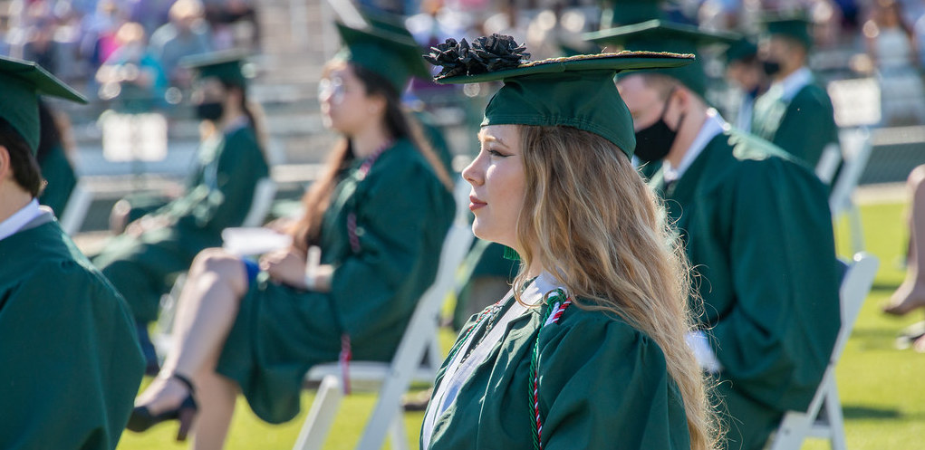 graduate sitting down wearing cap and gown during commencement 